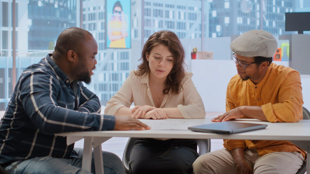 Three adults seated at a table reviewing documents and discussing plans in an office setting